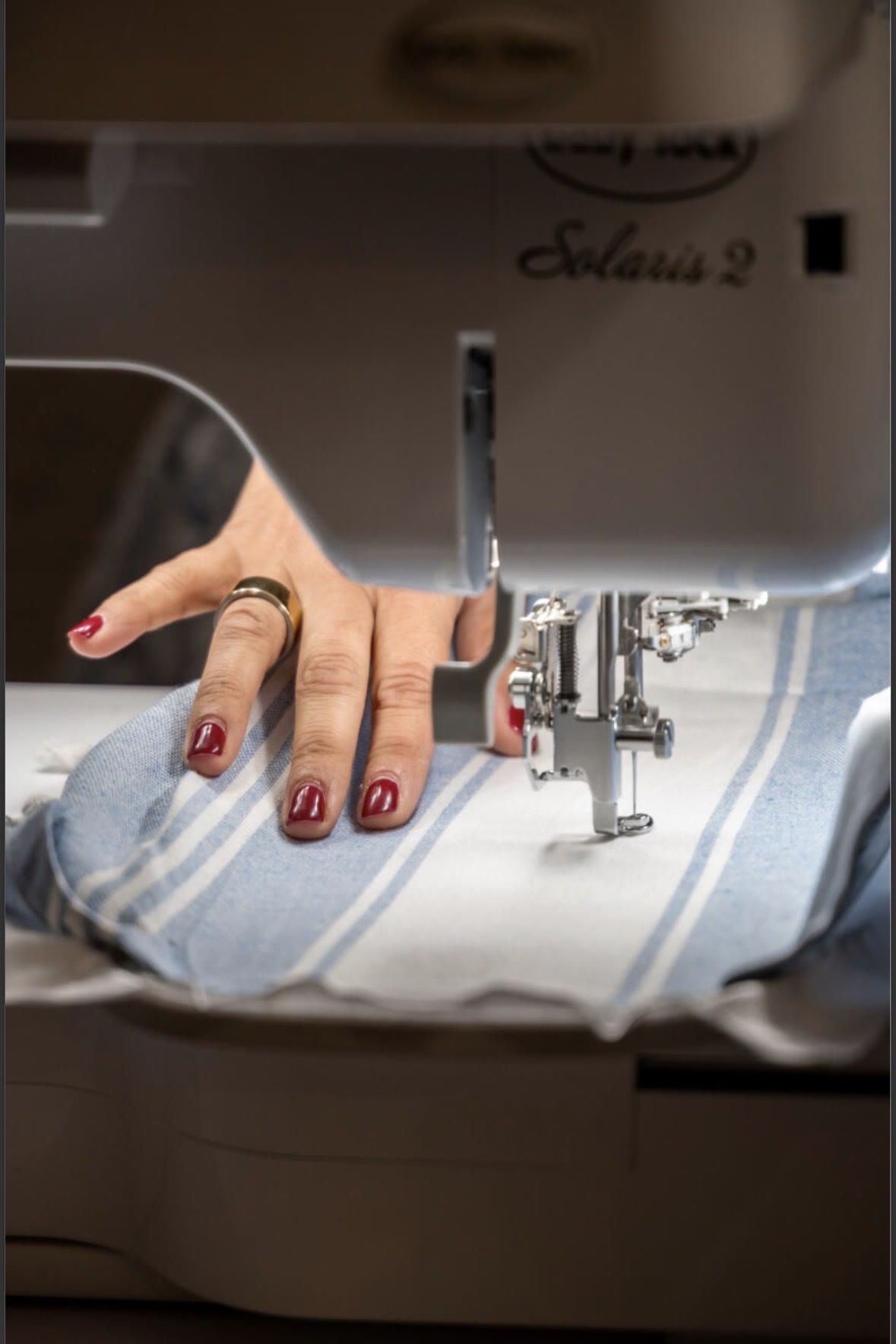 A hand guiding cabana-stripe fabric through the embroidery machine